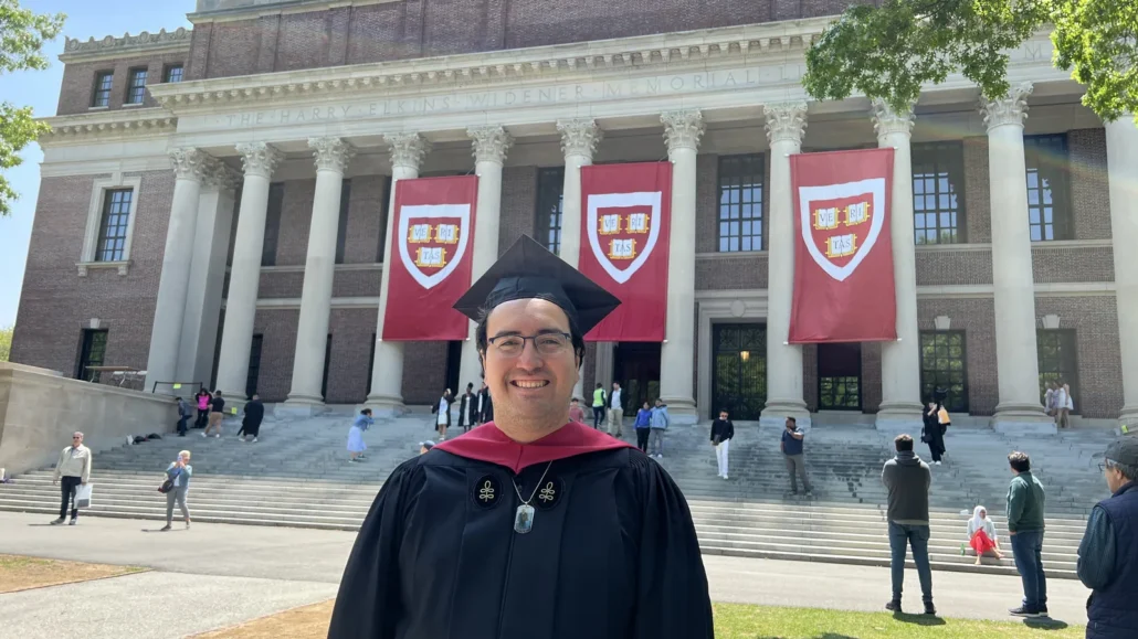 Sebastián Cisterna con toga y birrete frente a la biblioteca Widener, Harvard